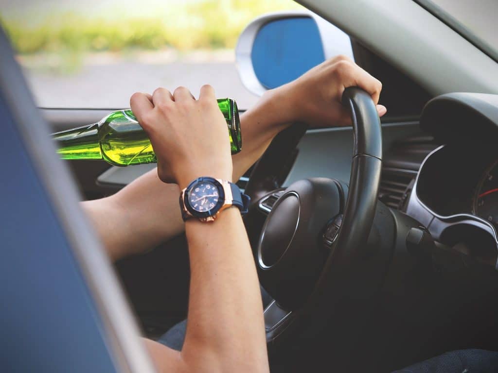 person with watch drinking beer while driving